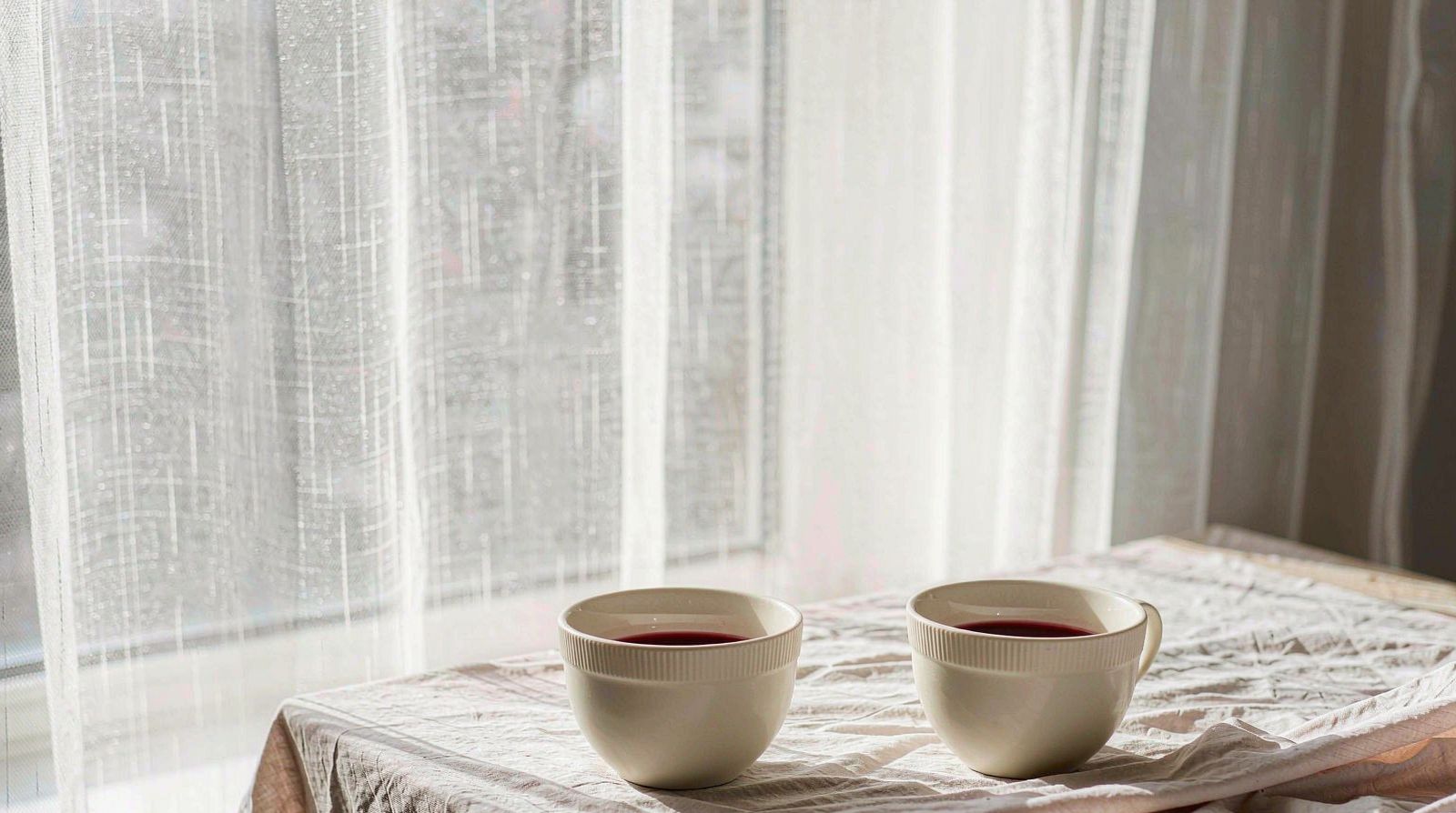 窗边亚麻桌布上的两只素色茶杯，晨光透过纱帘